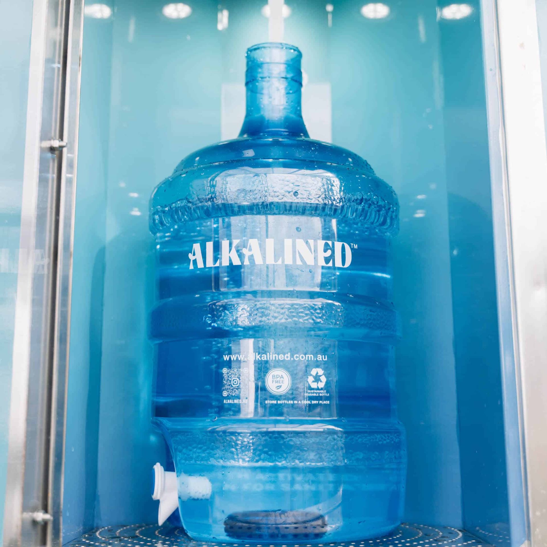 A bulk water bottle is being filled with alkaline water at an Alkalined fill station.