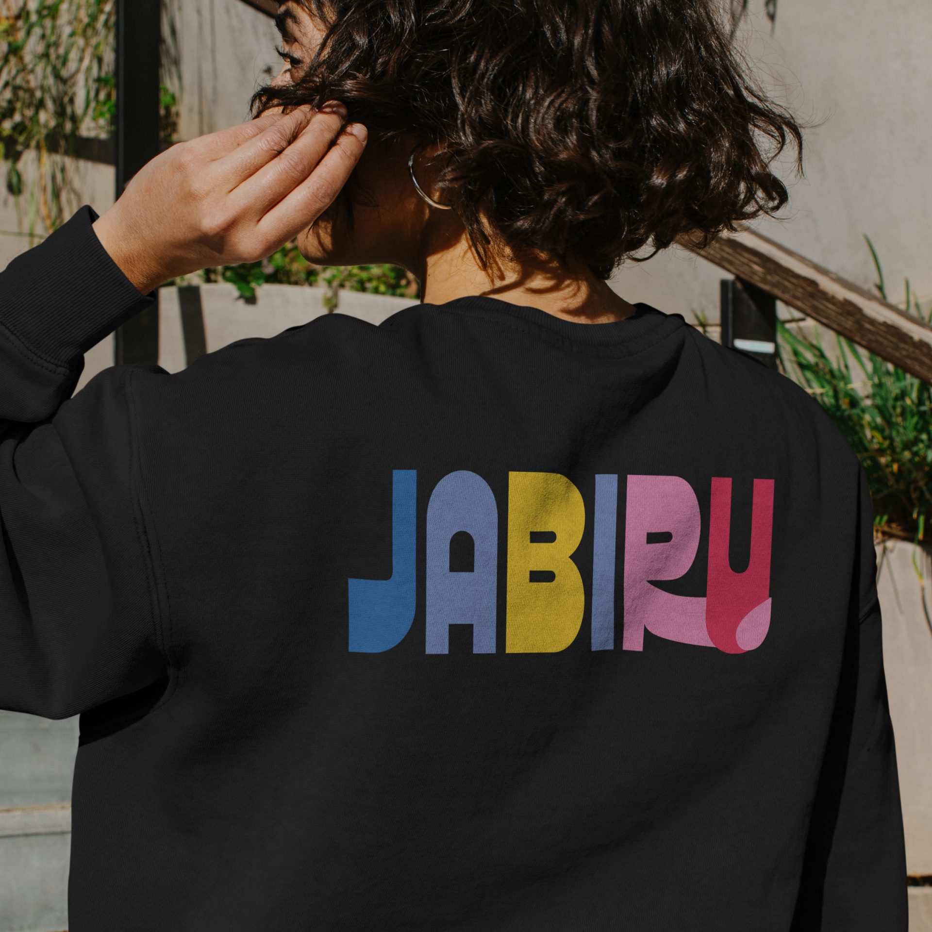Girl wearing a sweatshirt showing custom logo design for Jabiru Community College, featuring a bright, bold, clean aesthetic and queer-friendly rainbow tones.